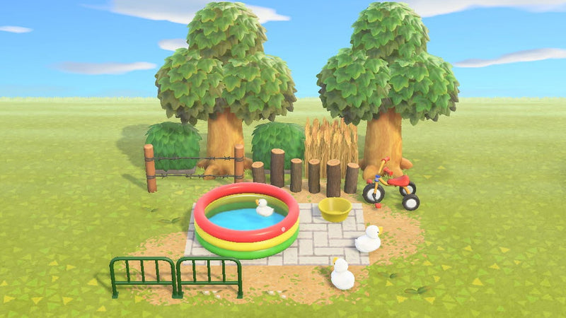 Animal Crossing Duckie Splash Pad room design with a colourful plastic pool, toy ducks, a yellow bath bucket and a red tricycle on stone paving, enclosed by barbed wire fencing, log stakes, hedges and hardwood trees